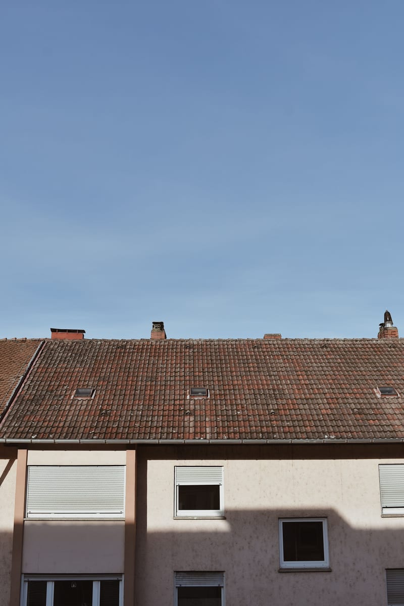 Weathered tile roof with several skylights beneath a clear sky